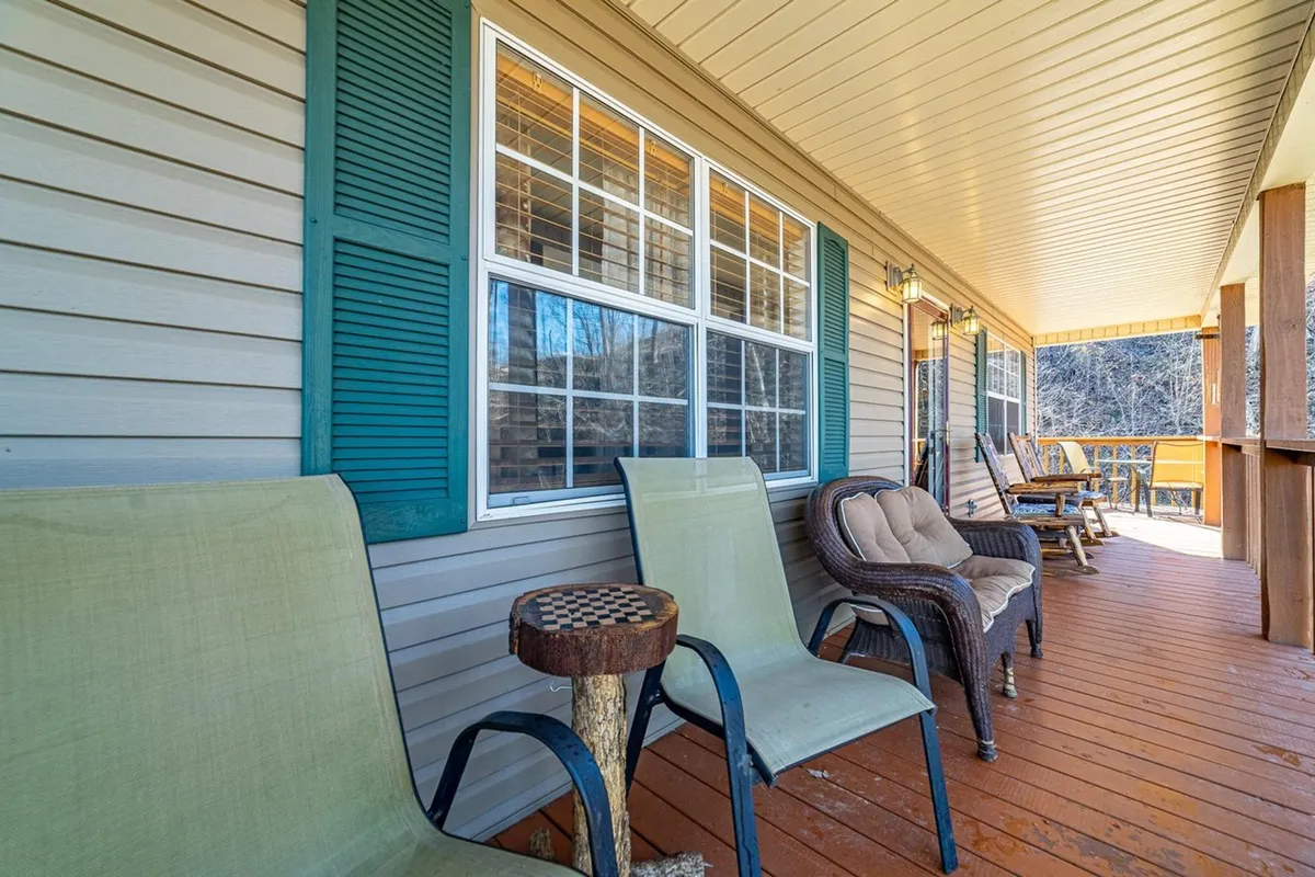 The photo presents a cozy outdoor seating area on a wooden porch, with comfortable chairs positioned to take in the surrounding greenery. The porch is adorned with homey details, such as window shutters and a view of the lush outdoors, suggesting a welcoming and sociable atmosphere perfect for morning coffee or sunset chats.