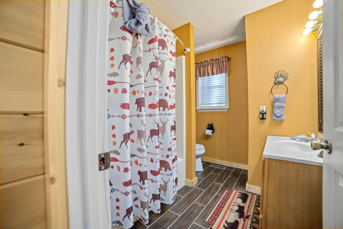 A well-lit bathroom featuring a shower curtain with animal prints, a wooden-accented vanity, and a window allowing in natural light. The space feels fresh, functional, and inviting—ideal for quick refreshes or unwinding before bed.