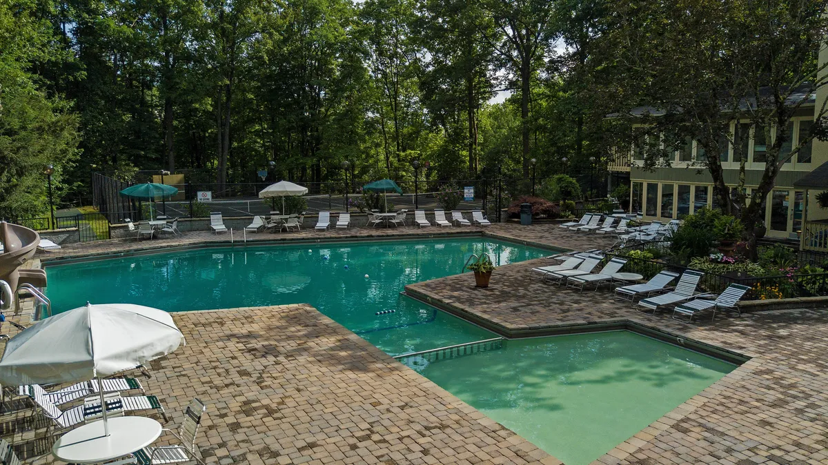 An inviting outdoor swimming pool surrounded by lounge chairs, umbrellas, and lush greenery, with guests swimming, socializing, and relaxing. The scene evokes a sense of community and leisure, perfect for both quiet mornings and lively gatherings.