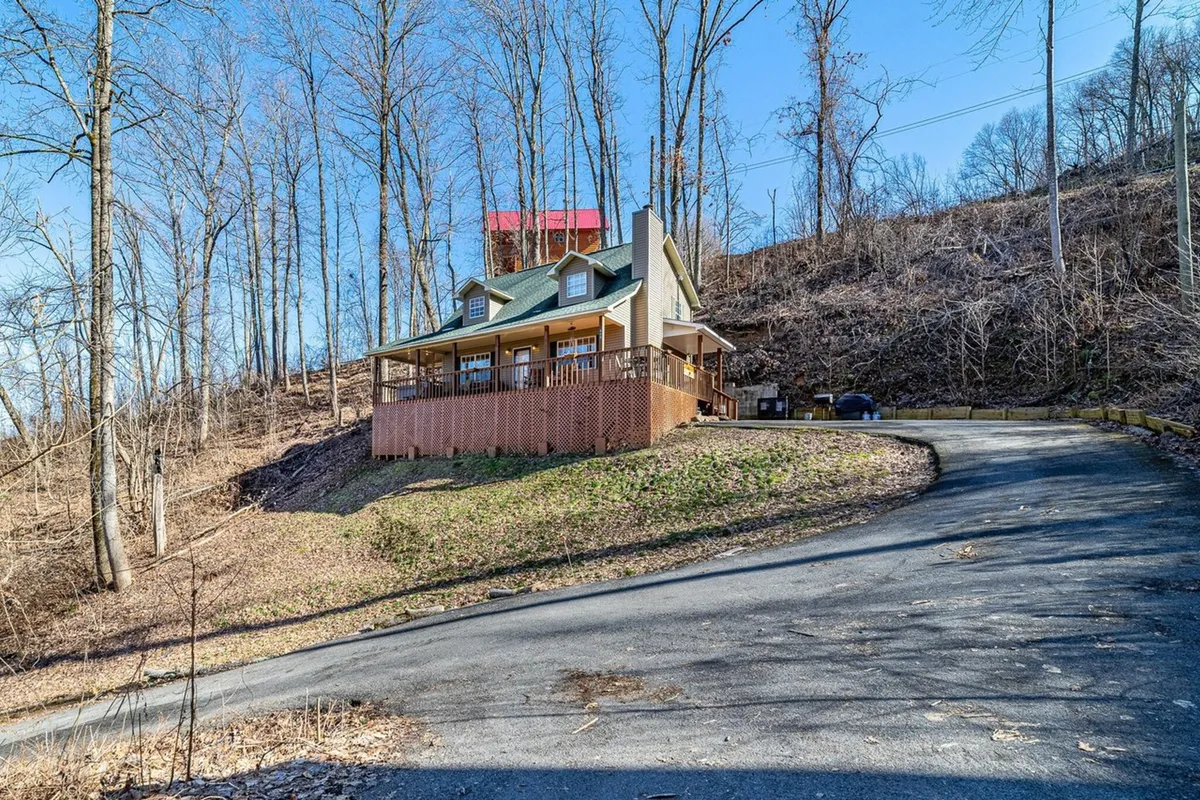 An exterior shot of the cabin with a spacious porch and a gently sloping driveway, surrounded by natural greenery. The view invites families to gather outdoors and explore nearby walking trails.