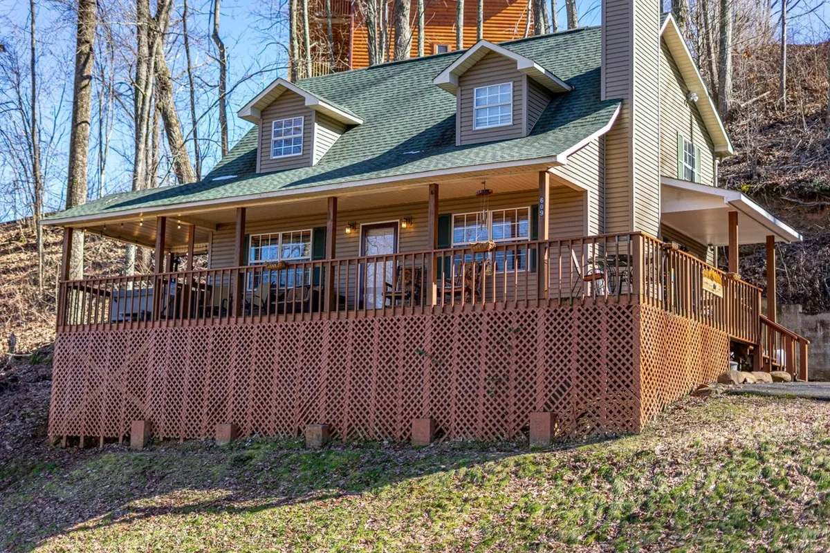 This image captures the front porch of the cabin, complete with wooden railing, a welcoming roofline, and landscaped surroundings. The space is designed for gatherings, with ample room for seating and outdoor relaxation, all set against the natural beauty of the mountains.