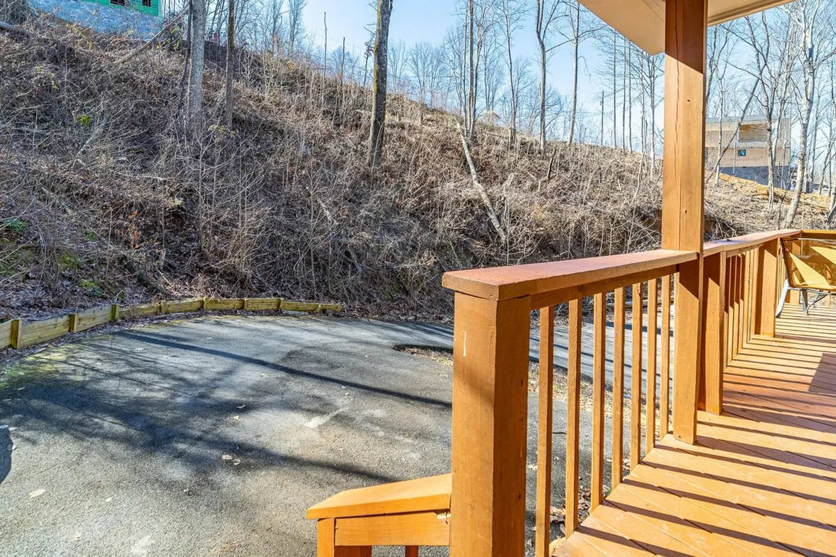 A serene view from a wooden porch overlooking a gravel driveway and wooded hillside, capturing the peaceful natural surroundings of the resort community. The space is perfect for relaxing with morning coffee or gathering after a day of adventure.