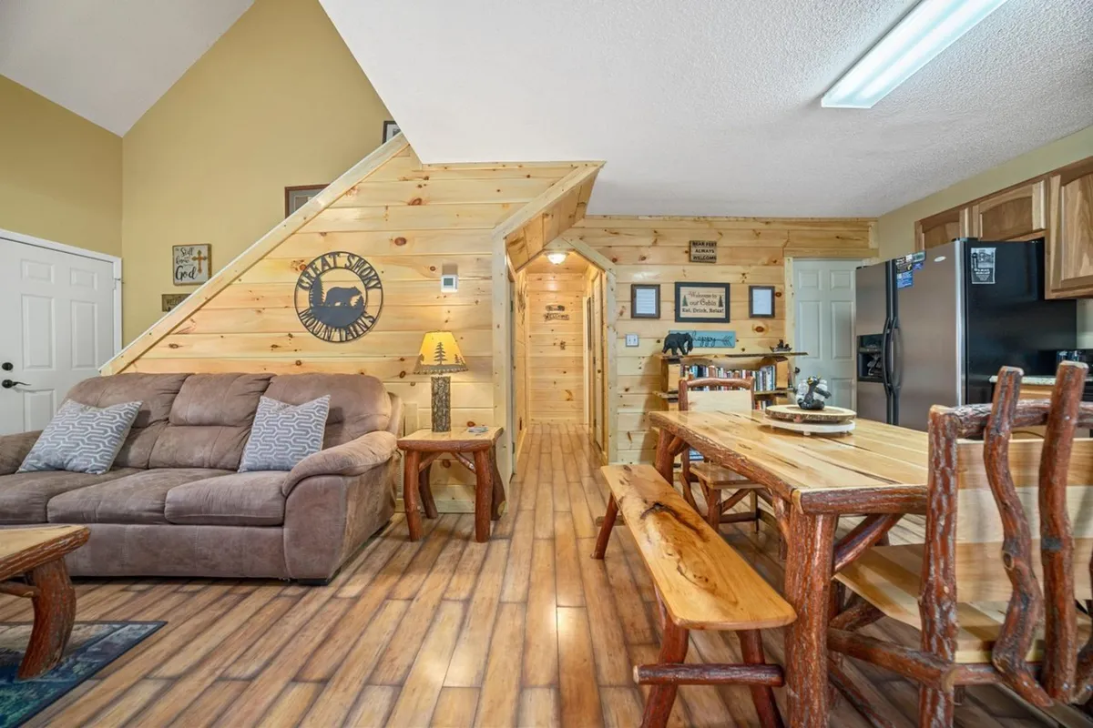 A cozy, homely great room showcasing a comfortable couch, wooden dining table, and decorative details. The space highlights areas for family meals, movie nights, and casual socializing, with a staircase leading to other parts of the chalet.