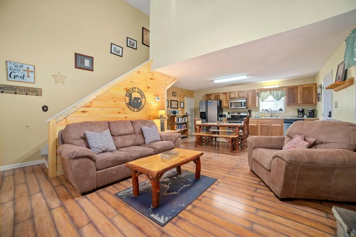 A bright, cozy interior view showing the seamless flow from a comfy sofa and coffee table to the open kitchen, with touches of rustic decor. The arrangement encourages casual conversations, game nights, and cooking together.