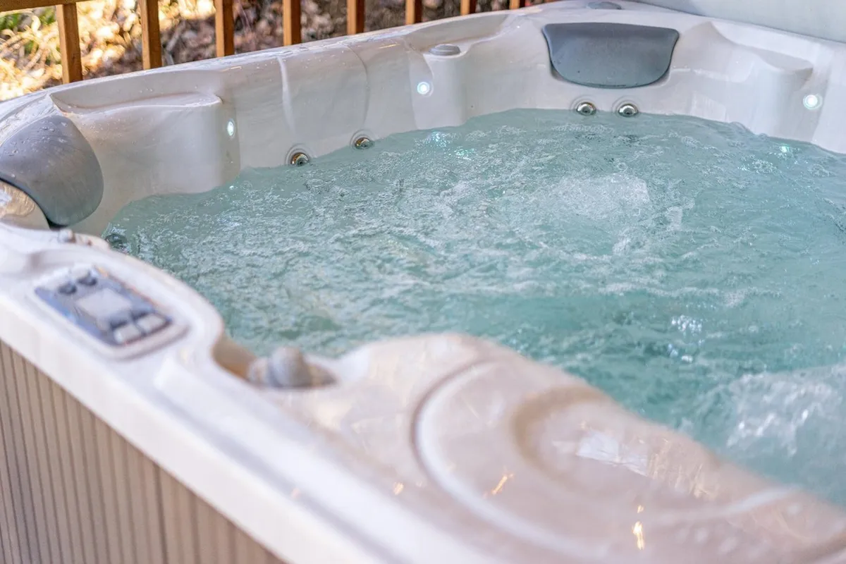 An inviting hot tub with bubbling water sits on an outdoor deck, suggesting relaxation and socialization under the open sky. The control panel indicates modern amenities, while the tranquil setting hints at mountain views beyond the frame.