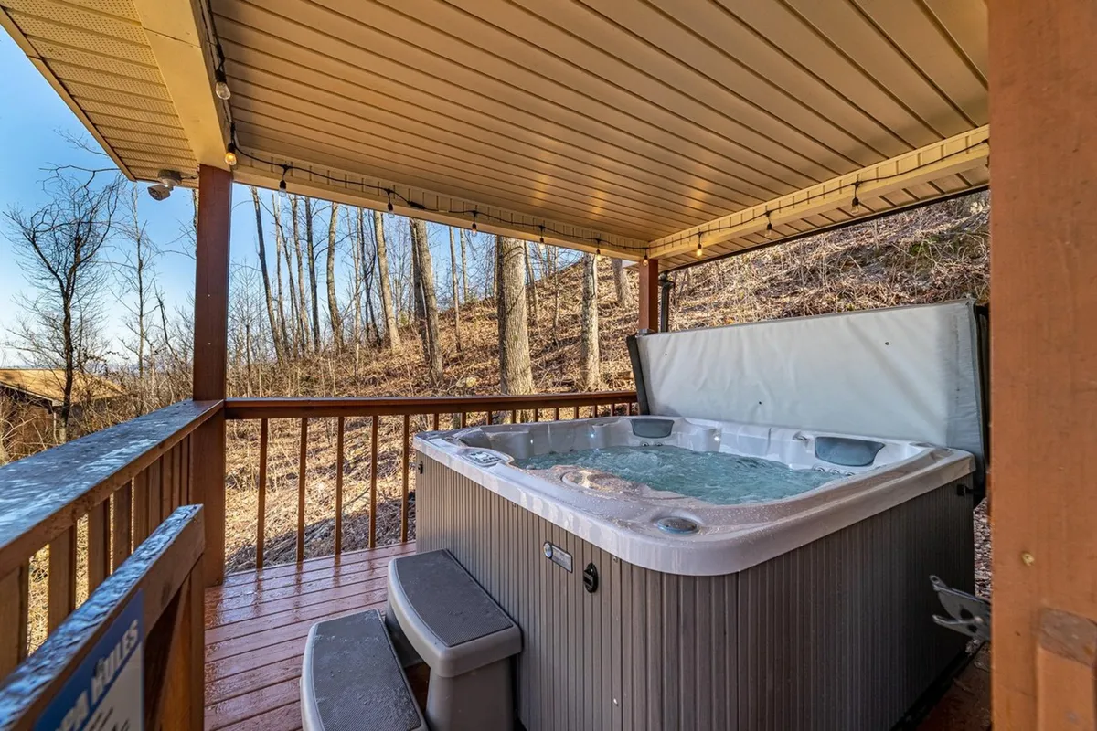 This image features a private hot tub situated on a wooden deck, surrounded by lush trees. The tranquil scene captures the experience of relaxing in the hot tub while taking in unobstructed views of the natural landscape, with ample space for socializing. The deck appears inviting, seamlessly blending comfort and immersion in the outdoors.